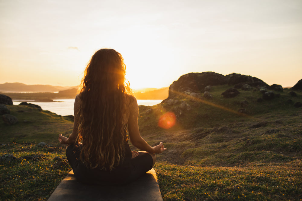 Woman meditating at sunrise to calm stress