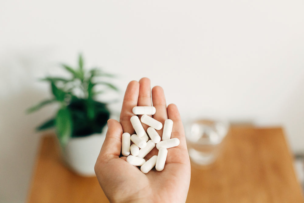Hand holding magnesium supplement capsules above a glass of water