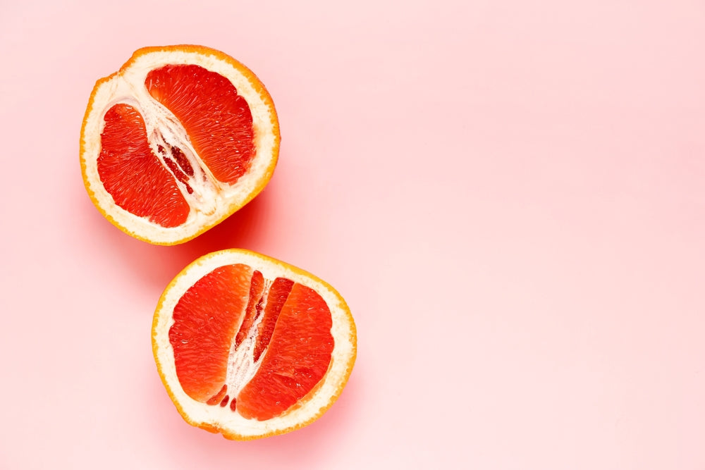 Two half of fresh red cut grapefruit on pink background. Female health concept. Fruit as symbol of vagina. Close up