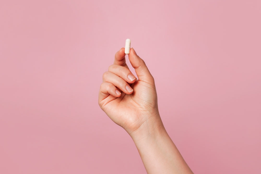 A hand holding a white capsule against a pink background
