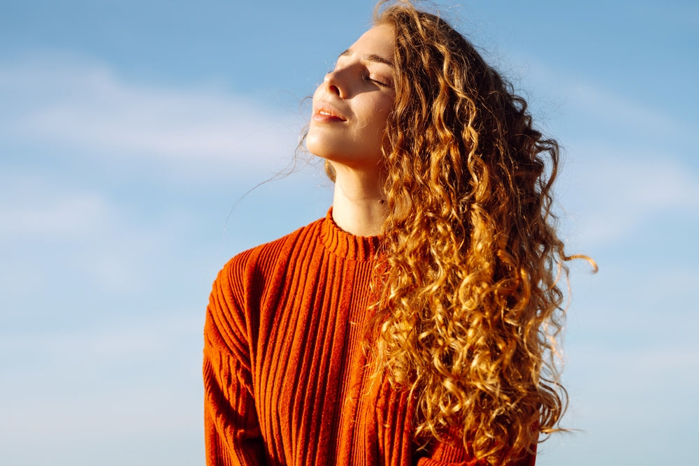 Portrait of relaxed woman enjoying wind in hair on sunny beach.