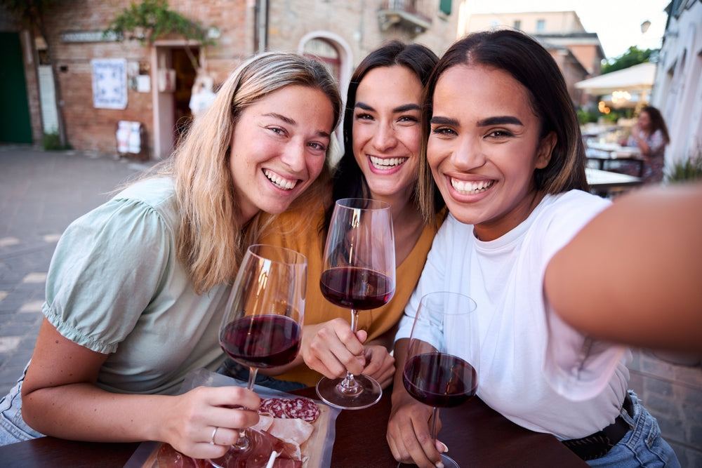 Three smiling multi-ethnic women are making a selfie while drinking red wine