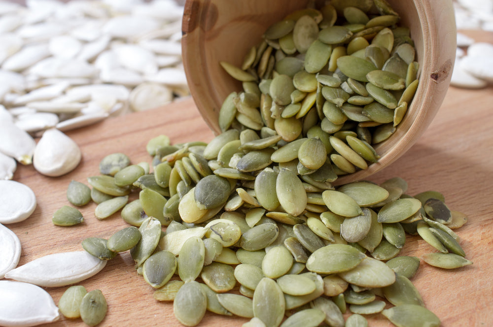 Peeled pumpkin seeds pour from a wooden cup